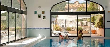 An indoor swimming pool with clear glass walls, a tiled floor, and a view of the outside.