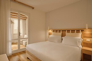 Ein Schlafzimmer mit einem Bett, Nachttischen, einem hölzernen Kopfteil und einer Glastür, die auf einen Balkon führt.