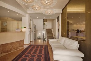 En moderne hotellobby med en receptionsdisk, en trappe, en hvid sofa og et mønstret tæppe.