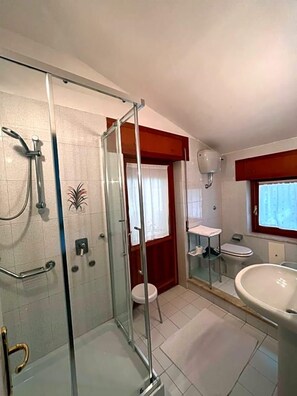 A bathroom with a glass shower enclosure, a toilet, a sink, and a window. - Hotel La Capannina (Aritzo)