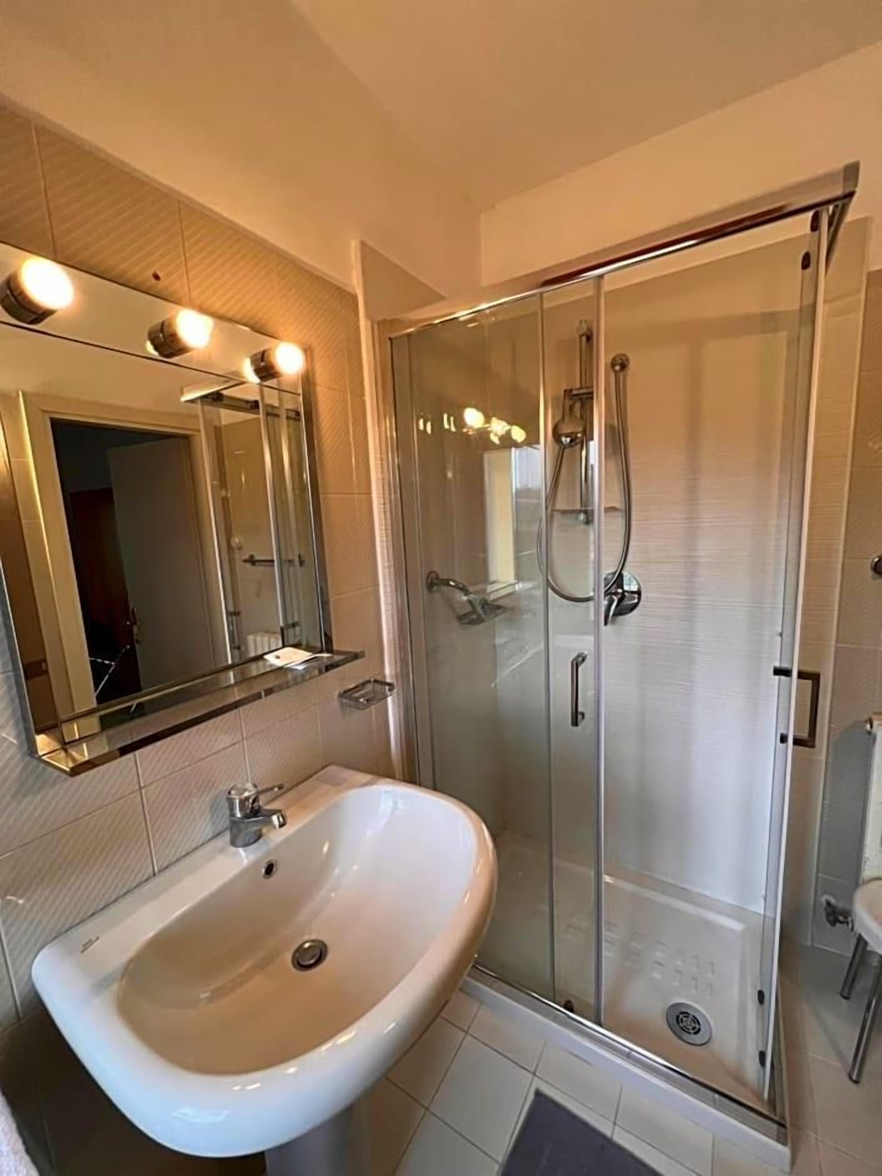 Un bagno con doccia vetrata, lavandino con specchio sopra e lampada a sospensione.