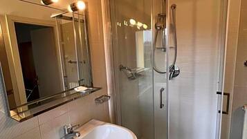 Un bagno con doccia vetrata, lavandino con specchio sopra e lampada a sospensione.