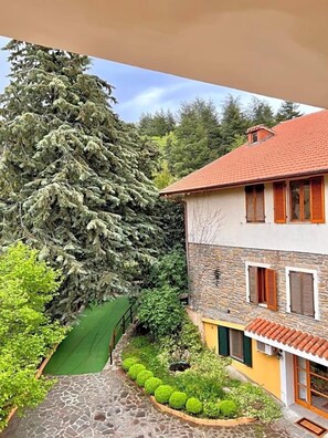 A two-story house with a stone facade, a red-tiled roof, and a large evergreen tree in the yard. - Hotel La Capannina (Aritzo)