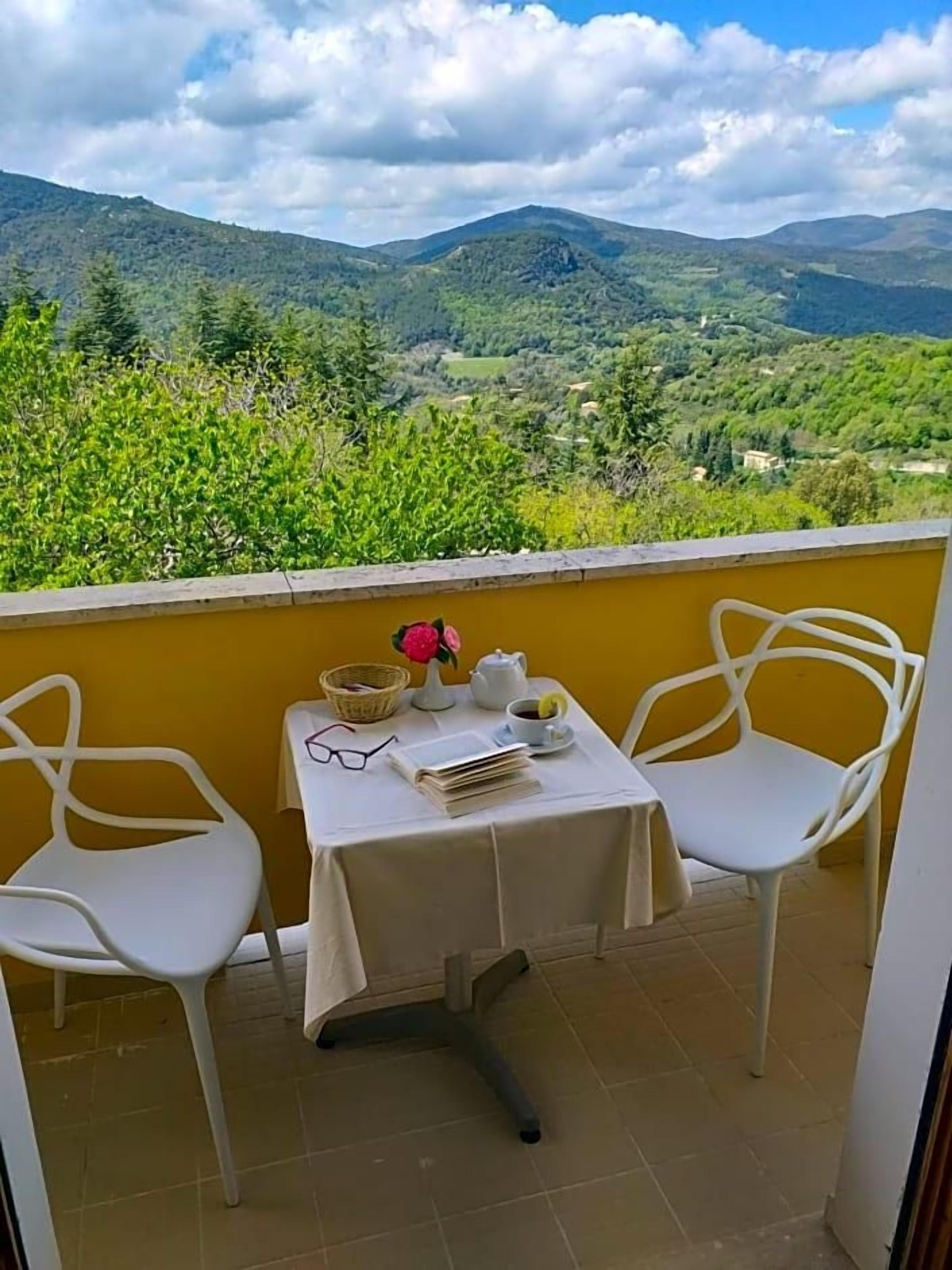 Un balcone con due sedie bianche e un tavolino, con vista su un paesaggio montuoso.