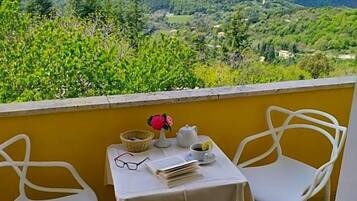 Un balcone con due sedie bianche e un tavolino, con vista su un paesaggio montuoso.