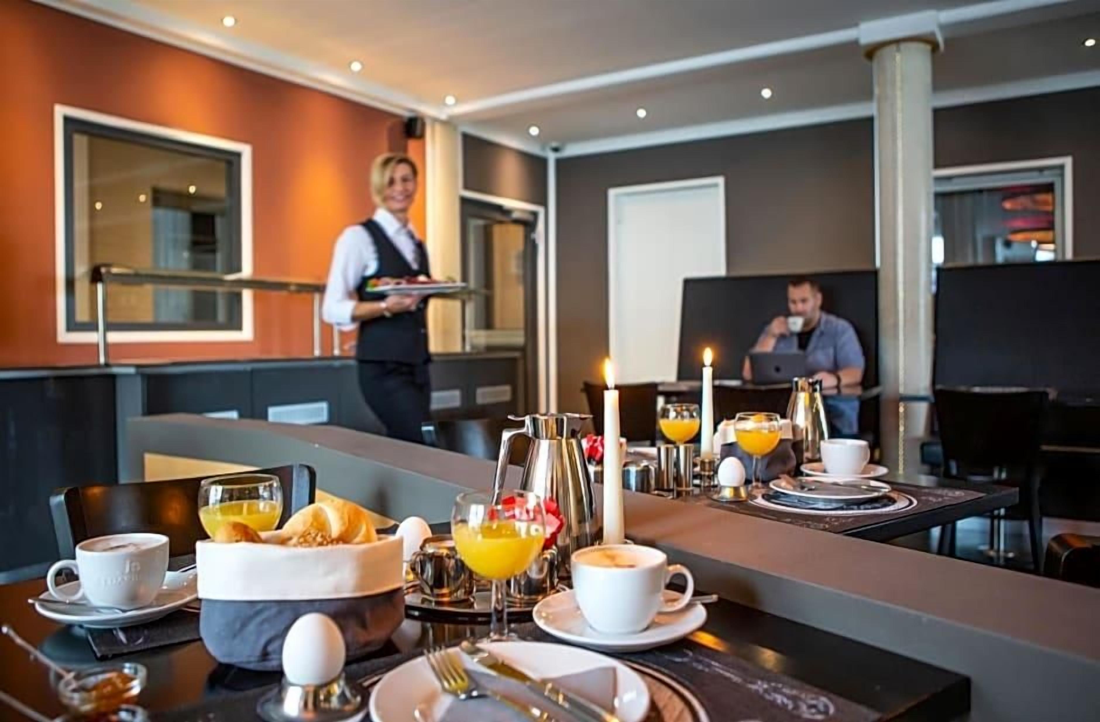 Ein Frühstückstisch mit Speisen und Getränken, ein Kellner und ein Mann, der am Tisch sitzt.