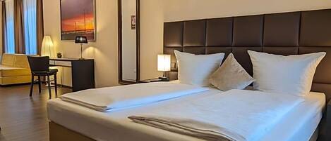 A hotel room with a large bed, a desk, and a chair.