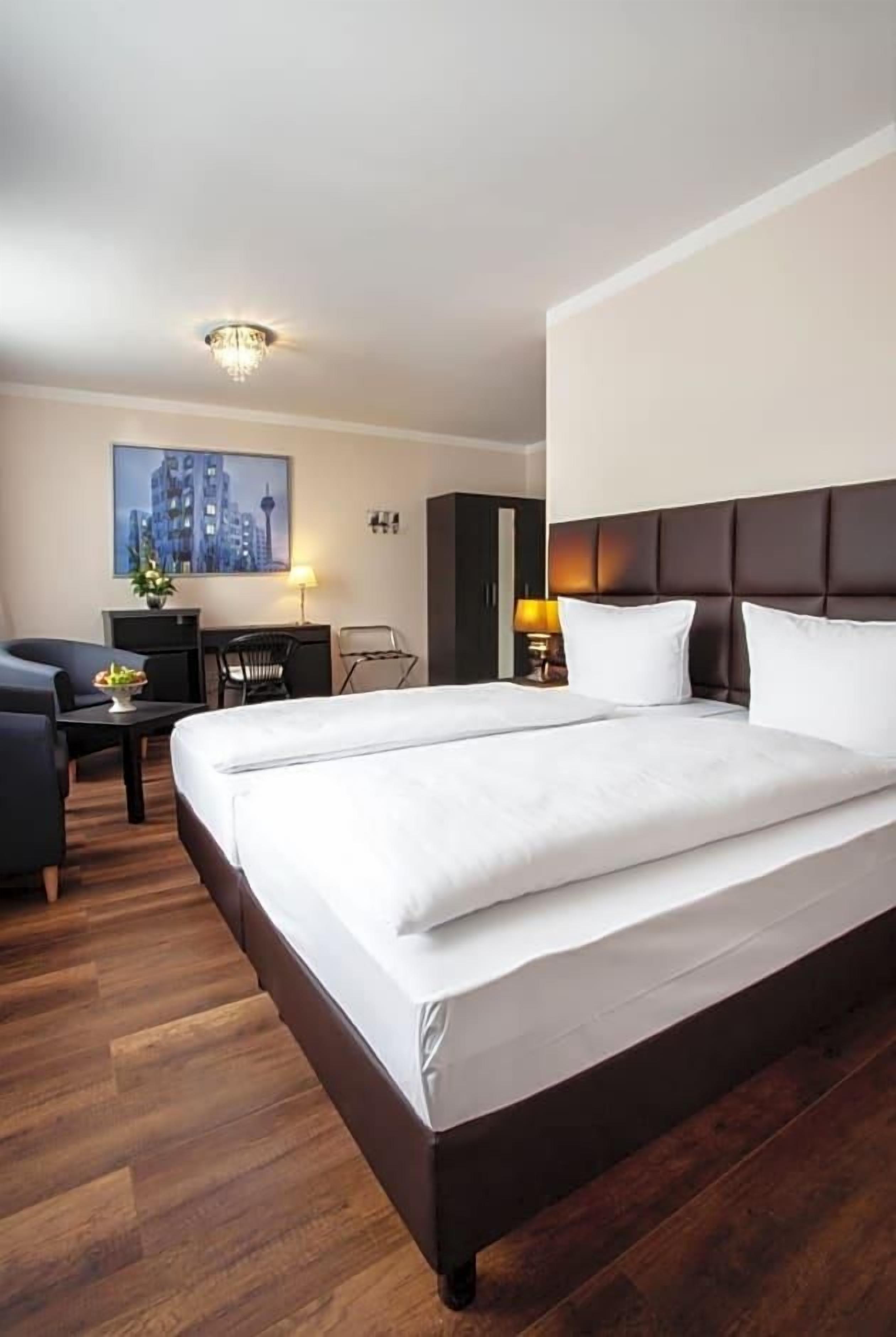 Ein Hotelzimmer mit einem großen Bett, einem Schreibtisch, einem Sessel und einem Stadtbild an der Wand.