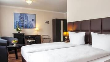 Ein Hotelzimmer mit einem großen Bett, einem Schreibtisch, einem Sessel und einem Stadtbild an der Wand.