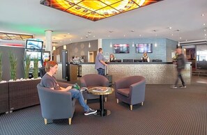 A modern hotel lobby with seating areas, a reception desk, and a large TV screen. - Hotel Royal Jvºlich (Jülich)