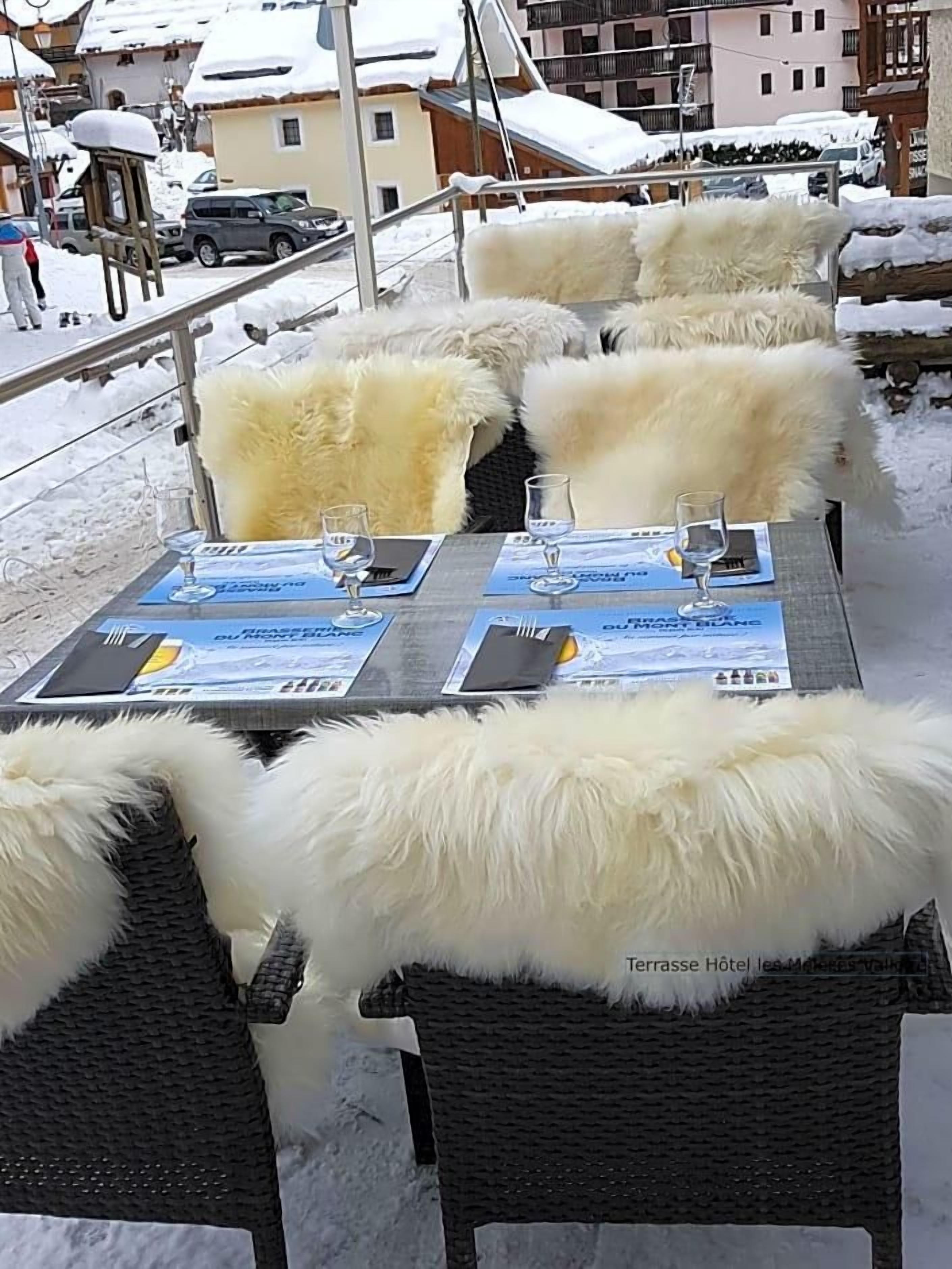 Tables pour les repas en plein air, avec des chaises recouvertes de fourrure, des menus et des verres.
