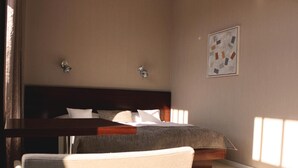 A bedroom with a bed, bedside tables, a chair, and a wall-mounted artwork. - Hotel Lev (Levice)