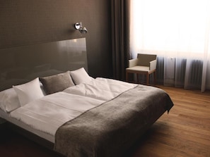 A hotel room with a large bed, a chair, and a window with curtains.