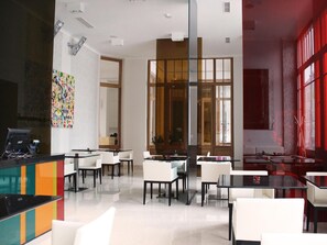 A modern hotel lobby with a reception desk, seating area, and large windows.