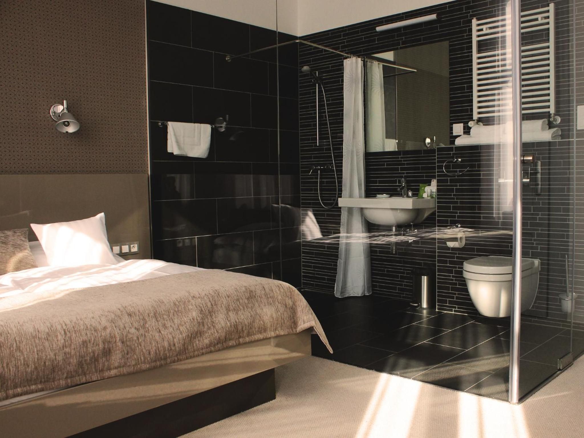 A modern bedroom with a large bed, a glass shower enclosure, and a bathroom with a sink and toilet.