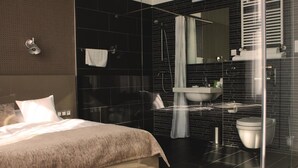 A modern bedroom with a large bed, a glass shower enclosure, and a bathroom with a sink and toilet. - Hotel Lev (Levice)