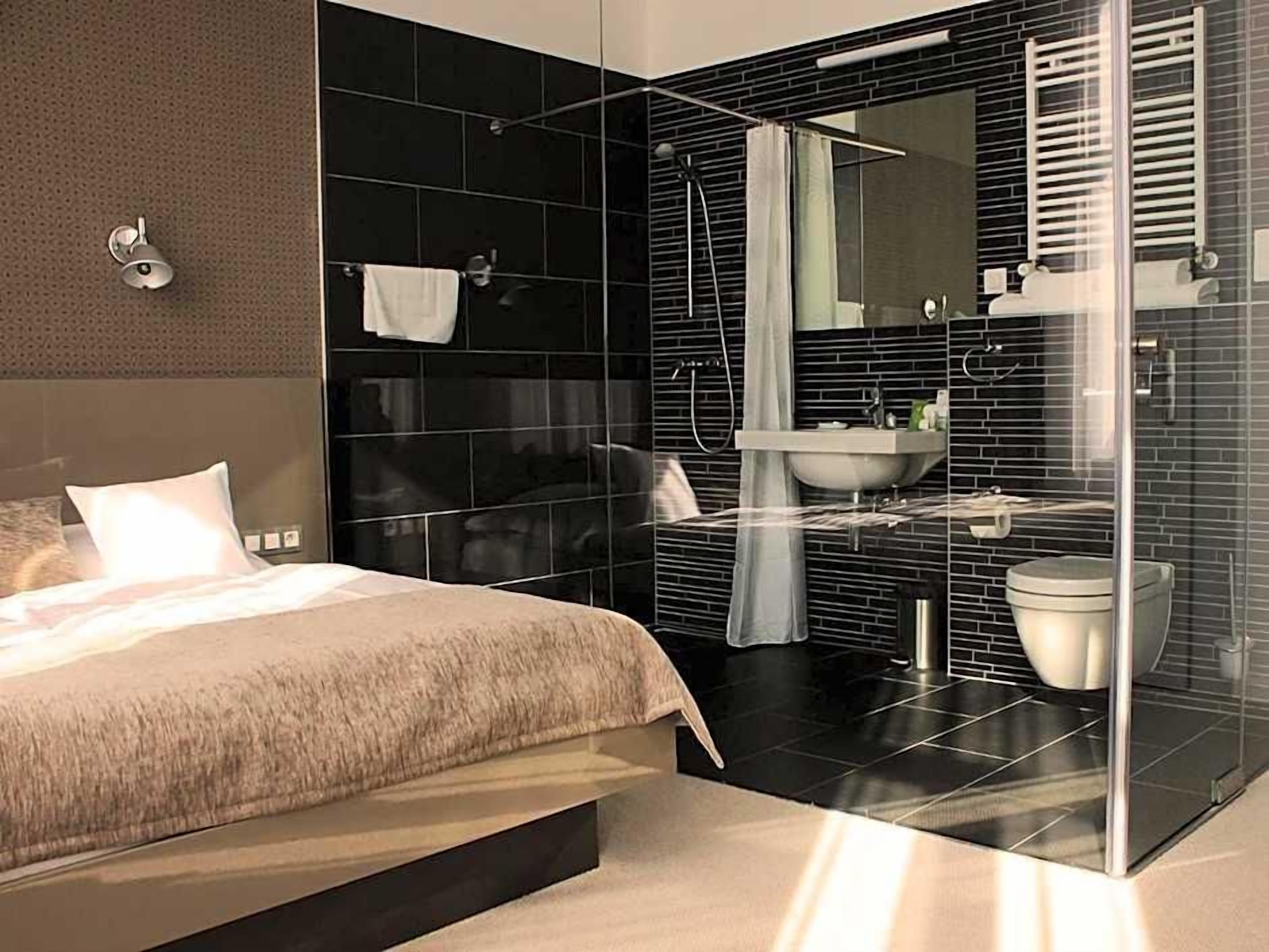 A modern bedroom with a large bed, a separate bathroom with a glass shower enclosure, and a large mirror.