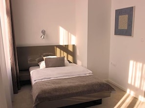 Quarto com cama, mesa de cabeceira, luminária na parede e quadro emoldurado.