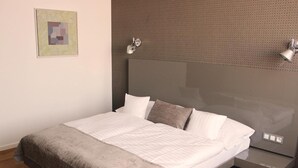 A modern bedroom with a large bed, a headboard with integrated lighting, a bedside table, and a wooden floor. - Hotel Lev (Levice)