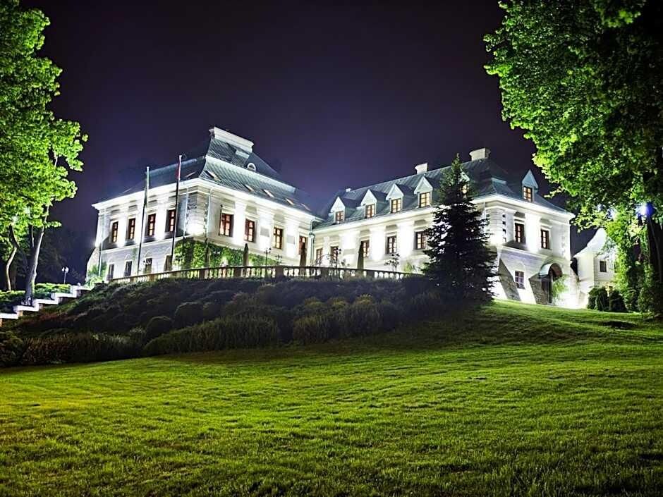 Een groot, verlicht gebouw met verschillende vleugels, omringd door een verzorgd gazon en bomen.