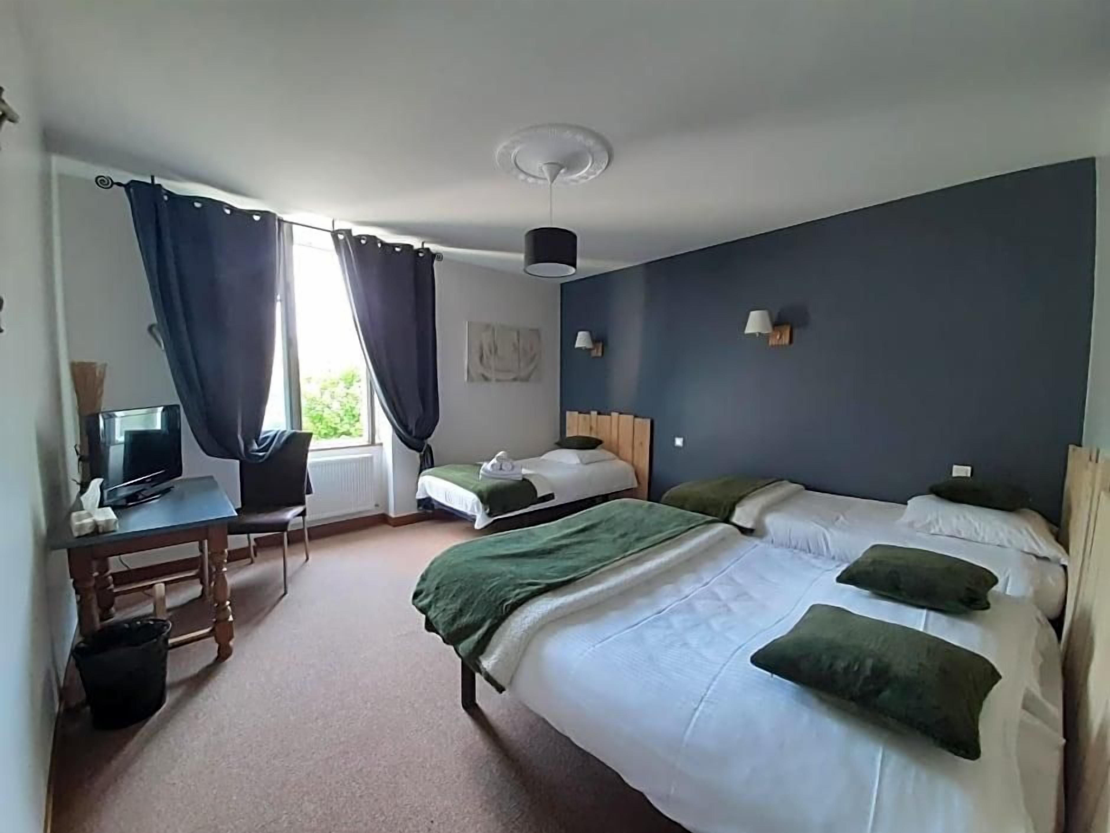 Une chambre d’hôtel avec un lit, un bureau avec un ordinateur, une chaise et une fenêtre avec des rideaux.