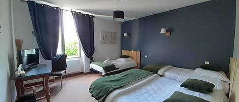 A hotel room with a bed, a desk with a computer, a chair, and a window with curtains.