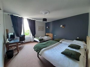 Quarto de hotel com cama, escrivaninha, computador, cadeira e janela com cortinas.
