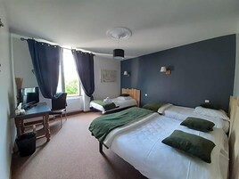 Quarto de hotel com cama, escrivaninha, computador, cadeira e janela com cortinas.