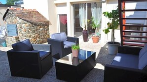 An outdoor seating area with sofas and a coffee table, surrounded by potted plants and a stone wall. - L Auberge Du Tire Bouchon (Couffé)