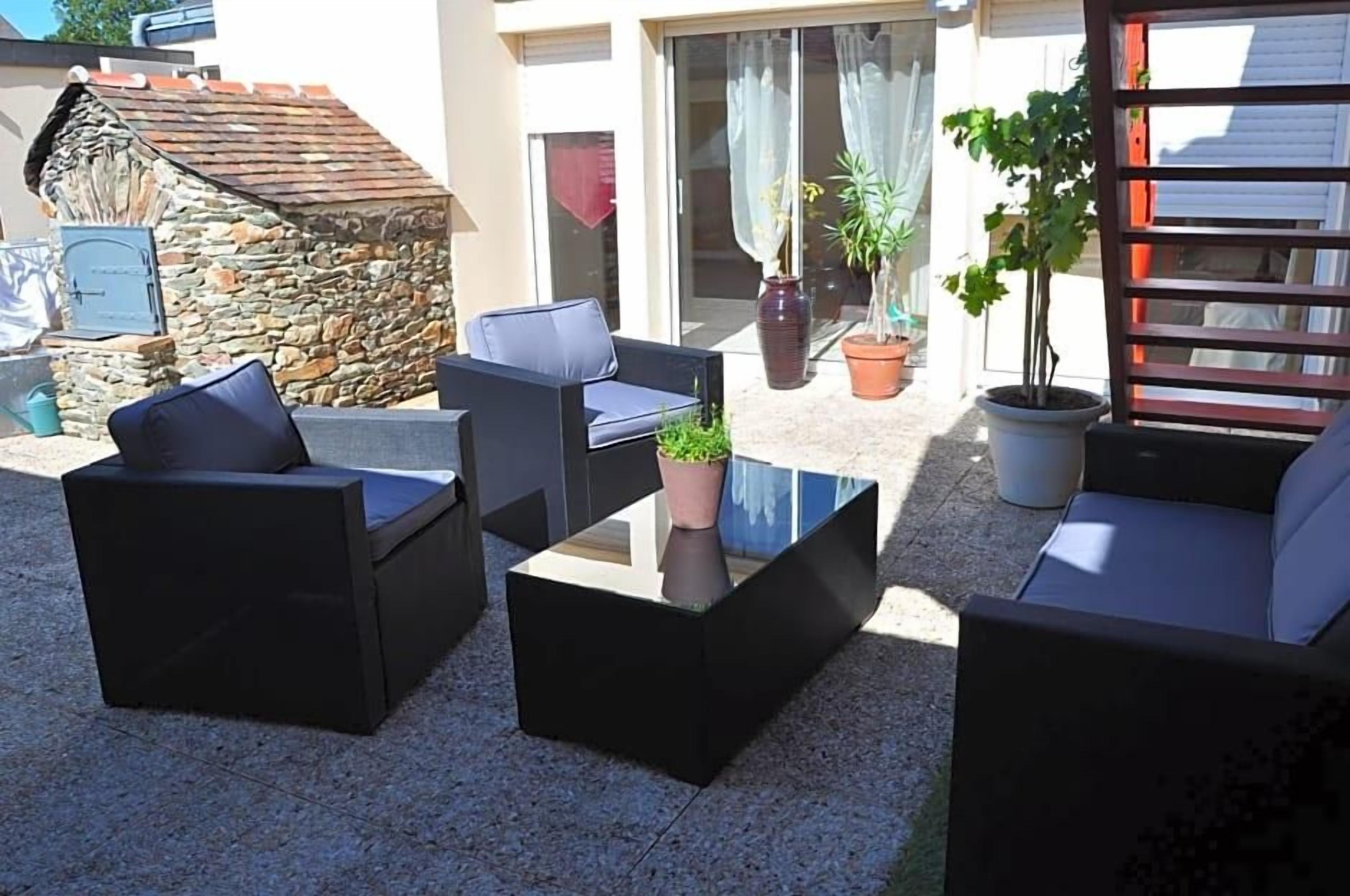 An outdoor seating area with sofas and a coffee table, surrounded by potted plants and a stone wall.
