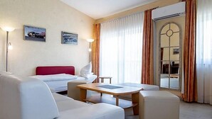 A hotel room with a bed, a sofa, a table, and a chair. There is a window with curtains and a door with a glass panel. - Land Gut Hotel Am Ring (Meuspath)
