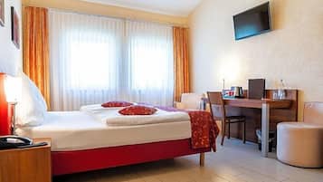 Ein Hotelzimmer mit Bett, Schreibtisch, Stuhl, Fernseher und einem Fenster mit Vorhängen.