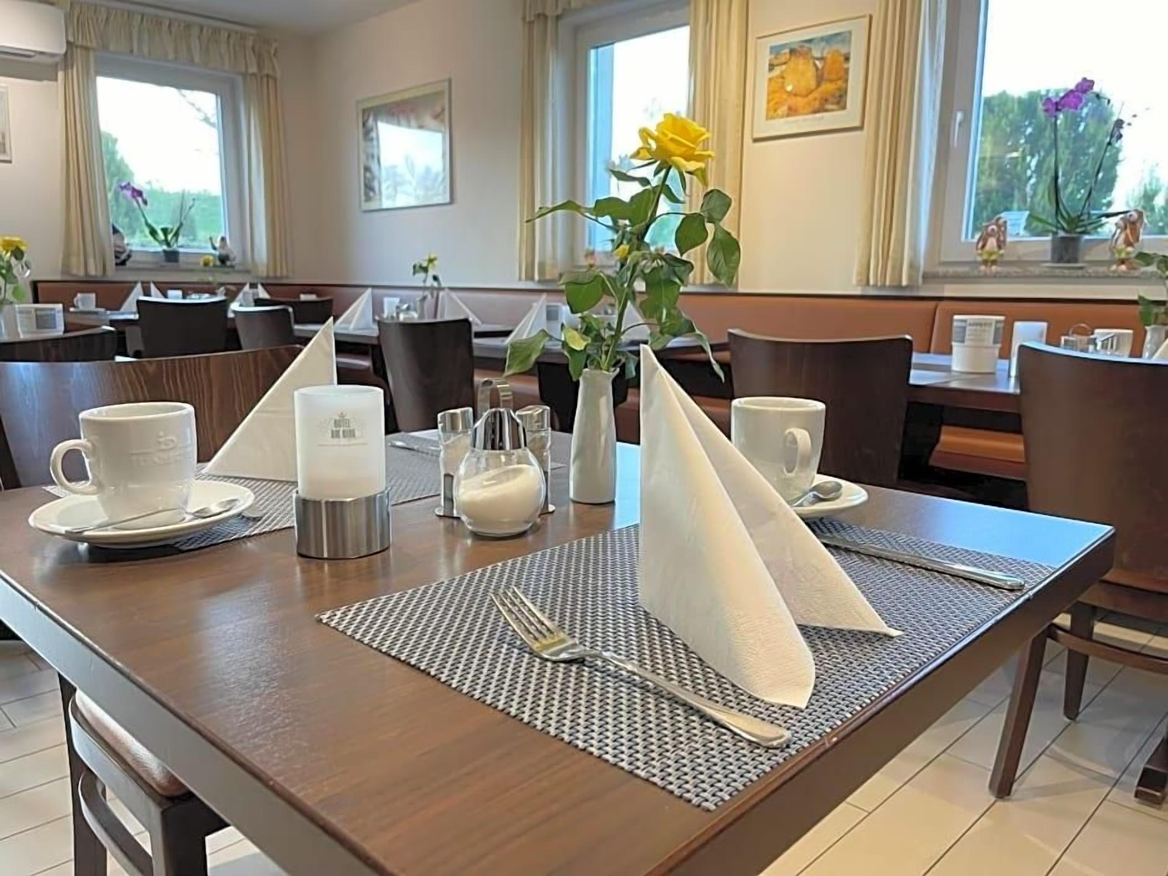 A dining area with tables set for breakfast, including cups, a pitcher, and a vase with flowers.