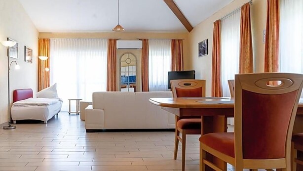A hotel room with a bed, a sofa, a dining table with chairs, a TV, and a window with curtains. - Land Gut Hotel Am Ring (Meuspath)