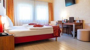 A hotel room with a bed, a desk, a chair, a TV, and a window with curtains. - Land Gut Hotel Am Ring (Meuspath)