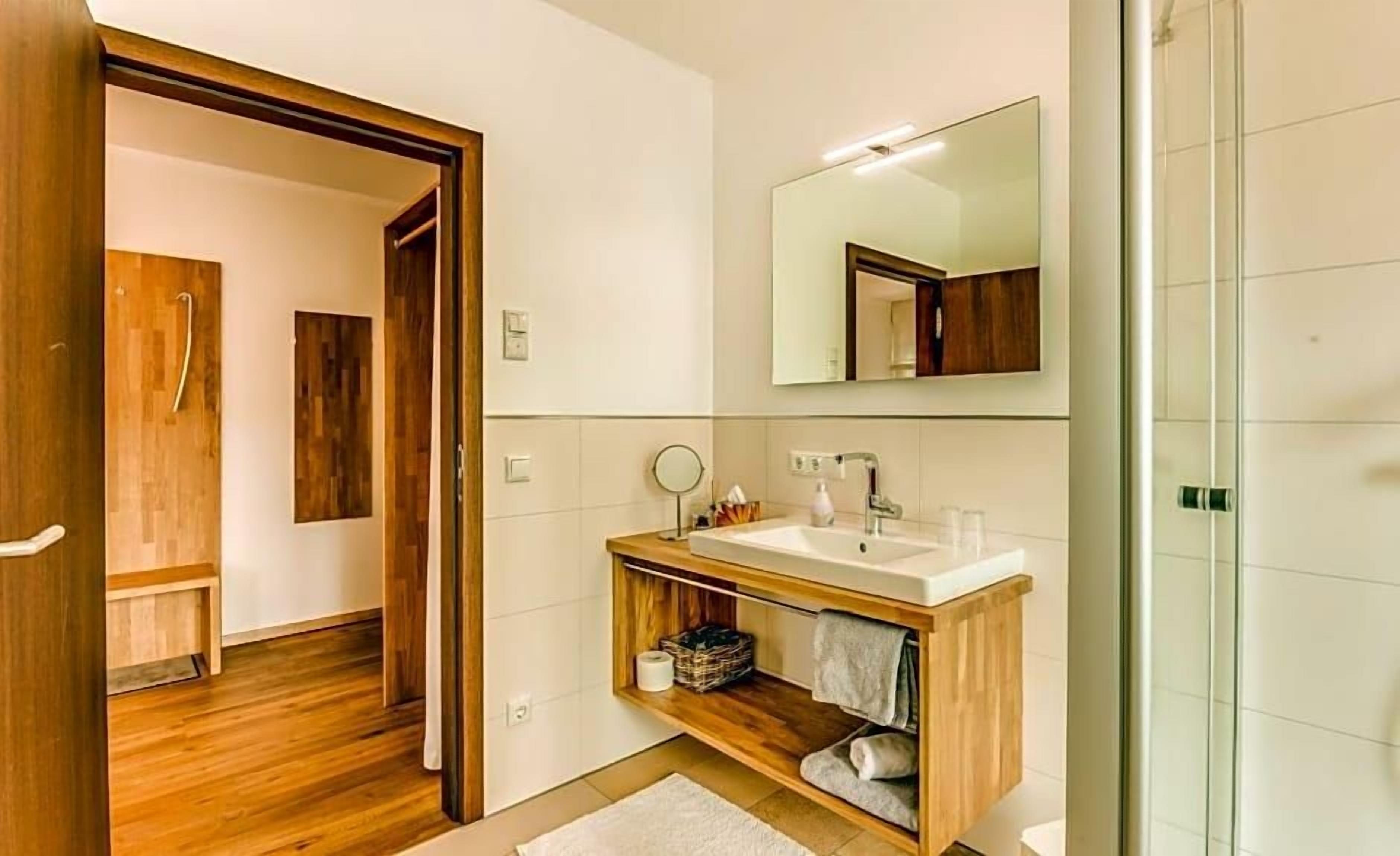 A modern bathroom with a wooden vanity, a large mirror, and a glass shower enclosure.