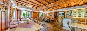 A spacious room with a wooden ceiling, a dining area with a long table, and a bar area with shelves. - Gasthof Schiesl (Altendorf)