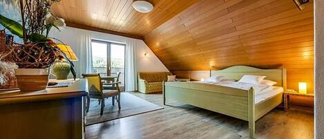 A bedroom with a sloped ceiling, a bed, a desk with a chair, and a window.