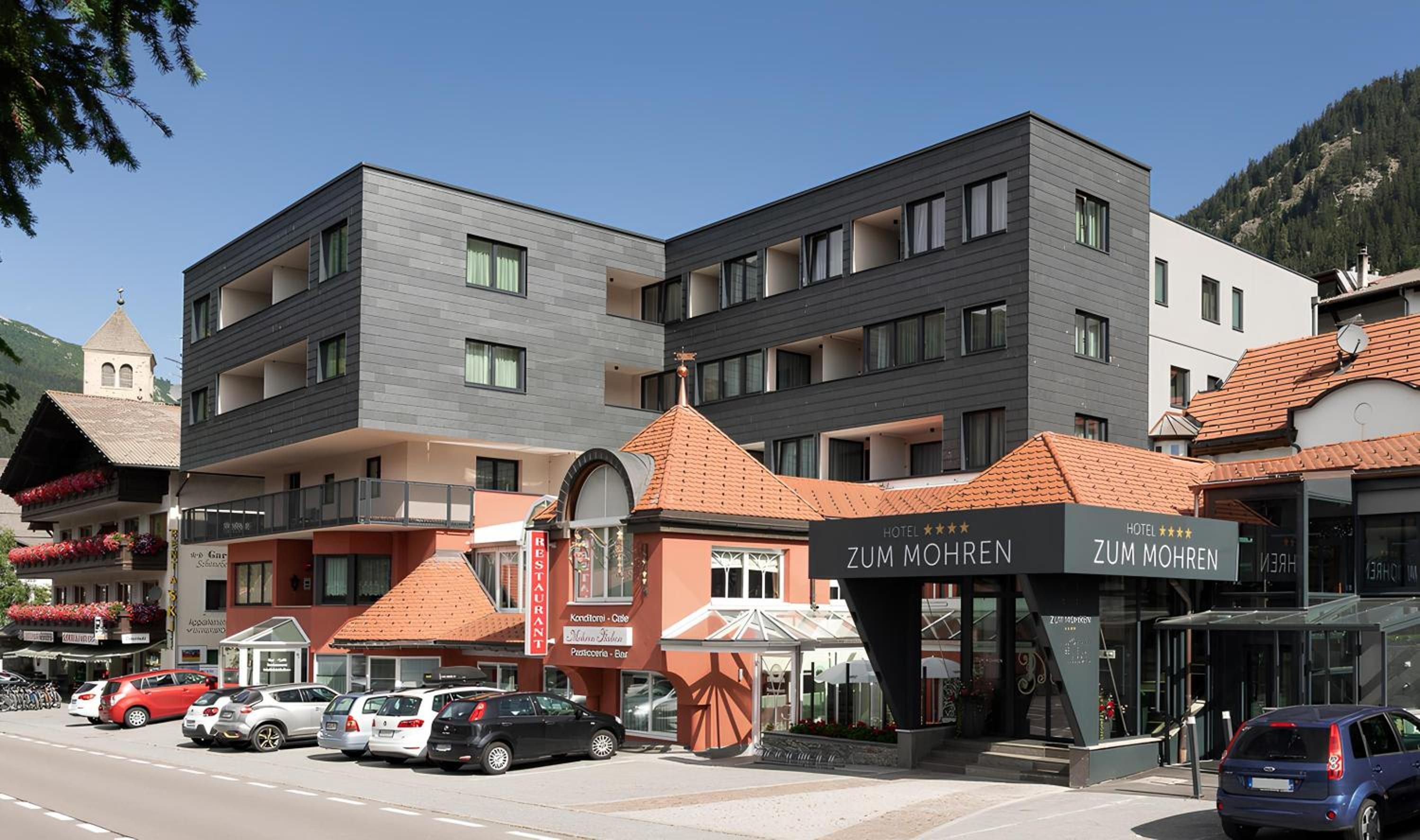 Un hotel con una facciata moderna, diversi balconi e un ristorante chiamato 'Zum Mohren' di fronte.