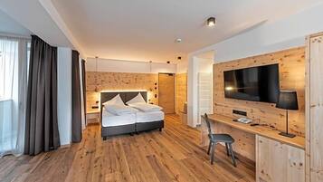 Ein modernes Hotelzimmer mit Holzboden, einem Bett mit weißen Leinentüchern, einem Schreibtisch mit Stuhl und einem am Wand montierten Flachbildfernseher.