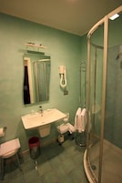 Un baño con lavamanos, espejo, toallero y ducha con mampara de vidrio.