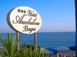 Señalización de 'Hotel Arabaleno Bagni' con vista al mar y sombrillas de playa.