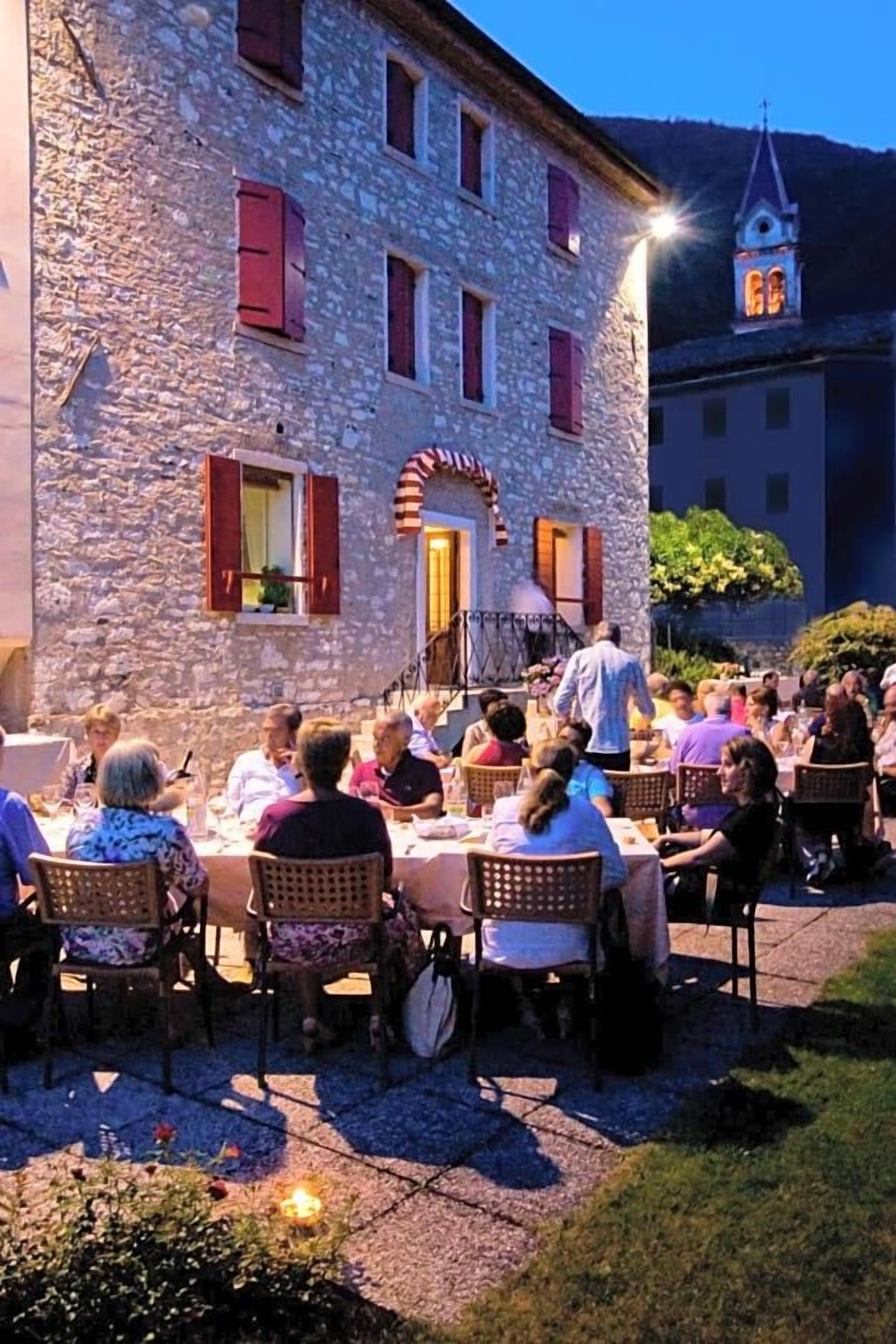 Un espacio de comedor al aire libre con edificios de piedra y la aguja de una iglesia al fondo.