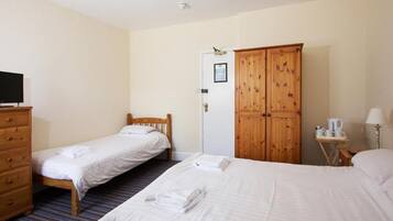A hotel room with two single beds, a wooden wardrobe, a television, and a small table with a lamp.