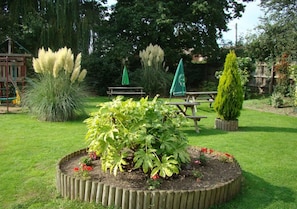 Un jardin avec un bac à fleurs en bois, une table de pique-nique et un parasol vert.