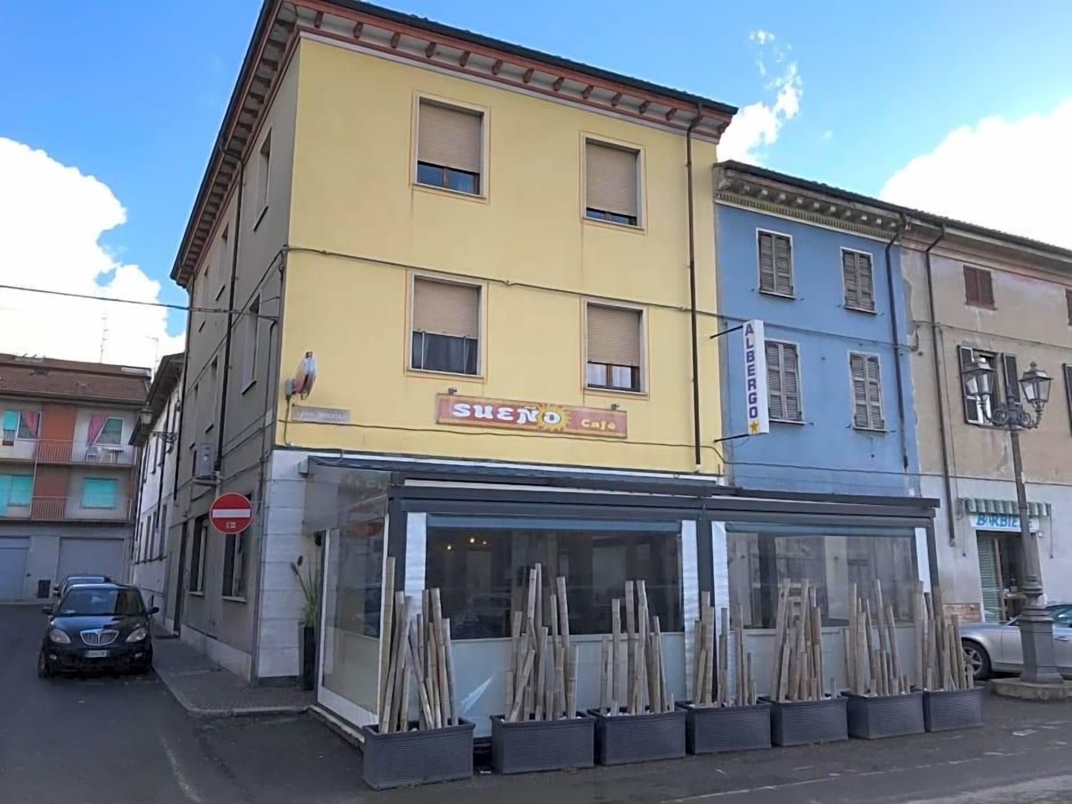 Ein zweistöckiges Gebäude mit einem Café im Erdgeschoss und einem Schild mit der Aufschrift 'ALBERGO' im zweiten Stock.