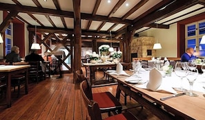 A restaurant with wooden beams, tables set for dining, and a fireplace in the background. - Weinhaus Henninger (Kallstadt)
