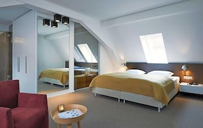 A modern bedroom with a bed, bedside tables, a red chair, and a small table with a candle. - Weinhaus Henninger (Kallstadt)