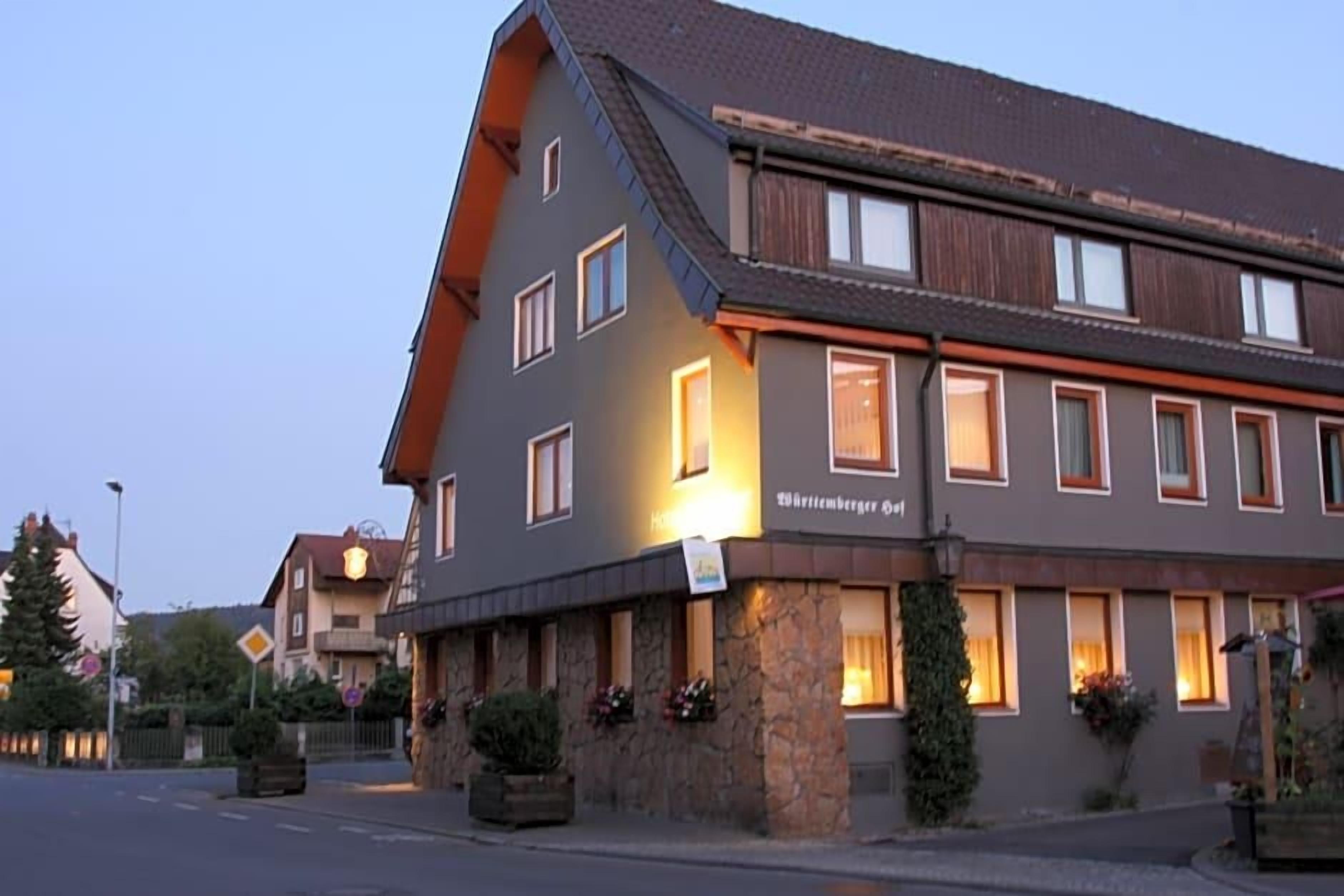 A hotel with a stone facade, multiple windows, and a sign indicating it is a 'Wirtshaus.'