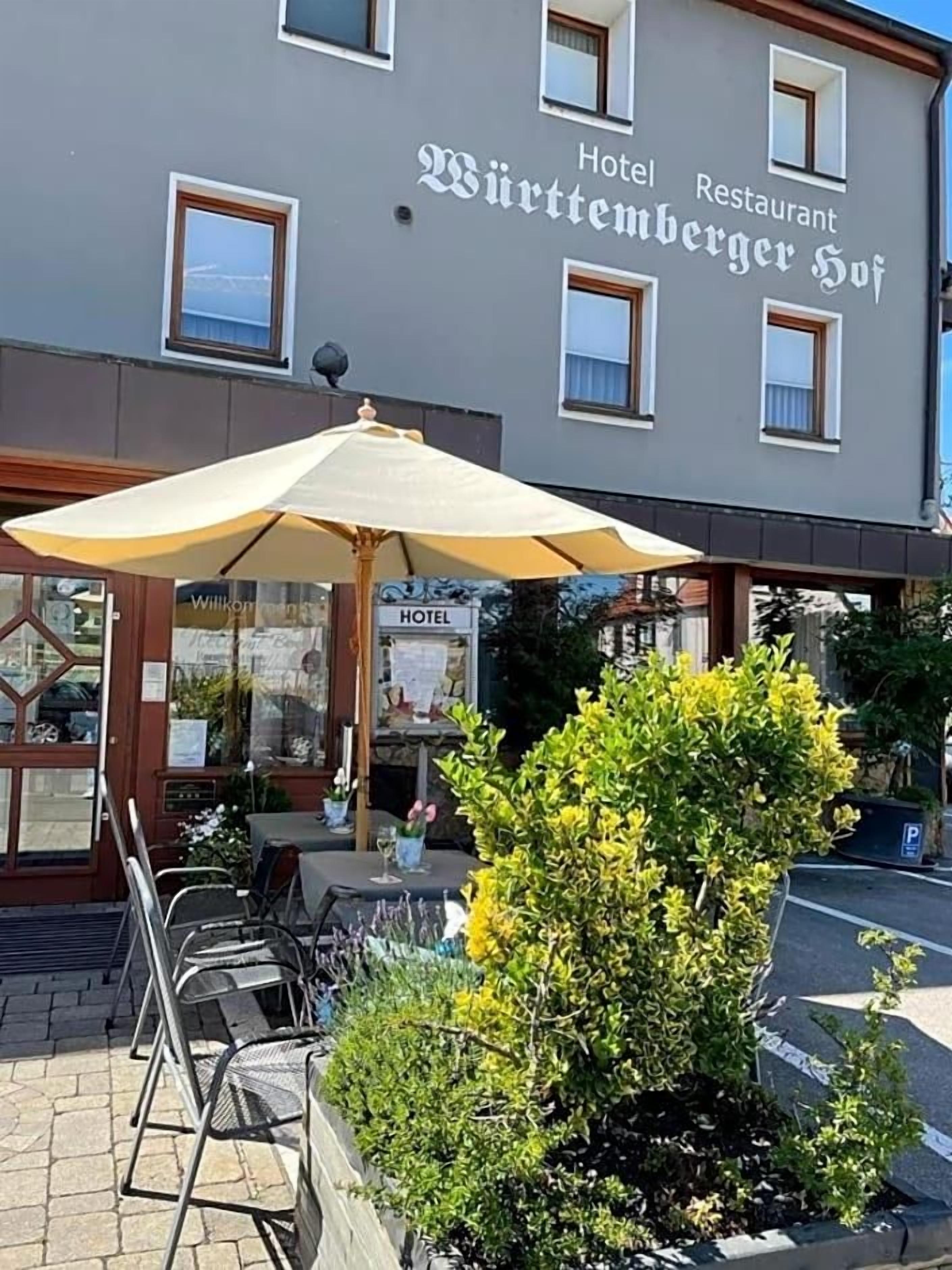 A building with a sign that reads 'Hotel Restaurant Württemberger Hof' and outdoor seating with umbrellas.